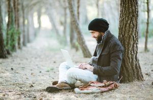 Man stiing under tree and working on laptop