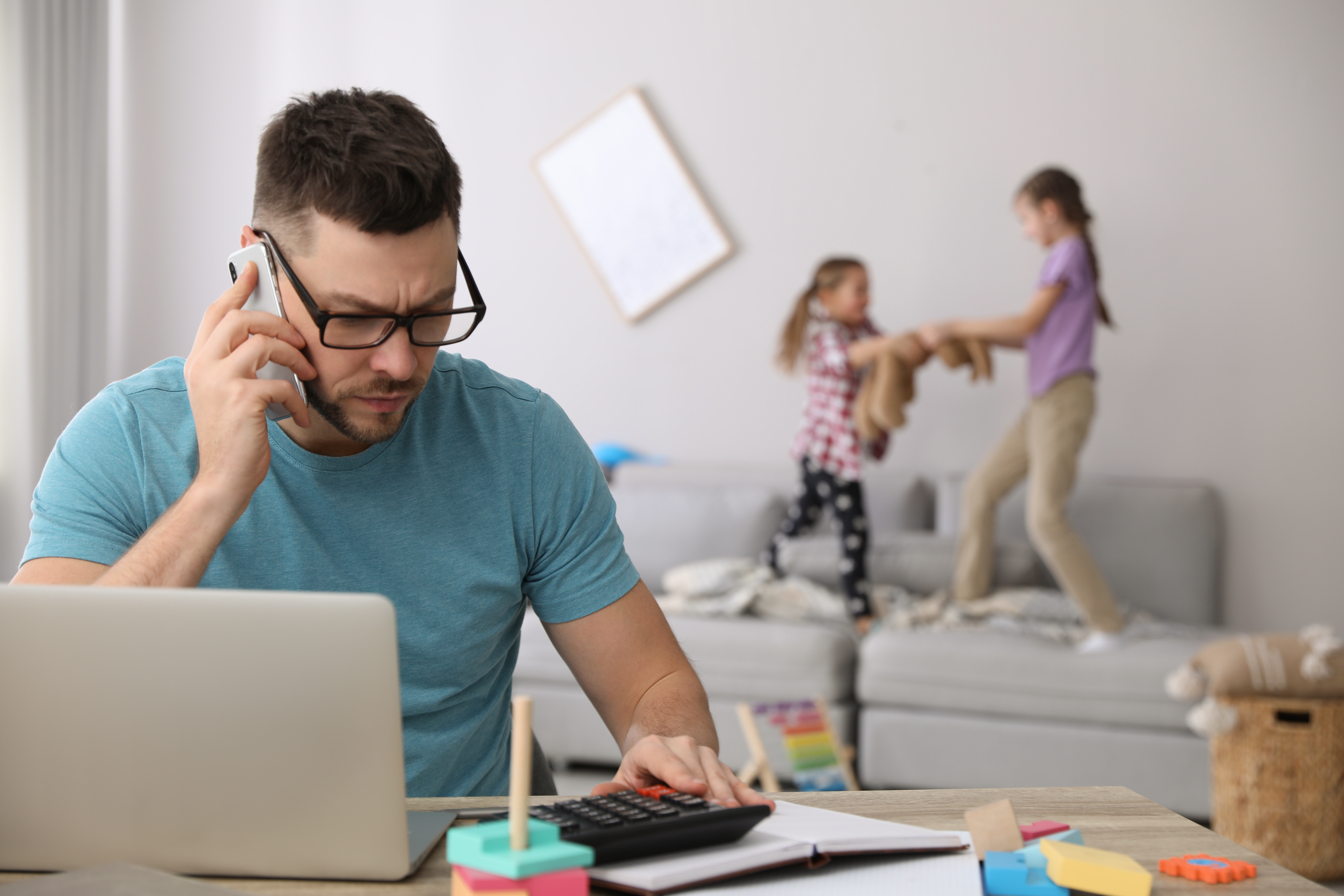 Children disturbing stressed man in living room. Working from ho