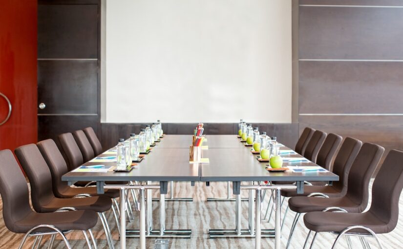 A meeting room set up with chairs, a table, water, fruit, and a screen.