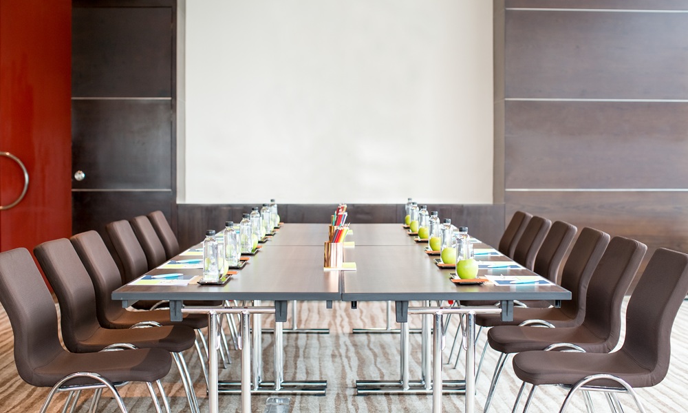 A meeting room set up with chairs, a table, water, fruit, and a screen.